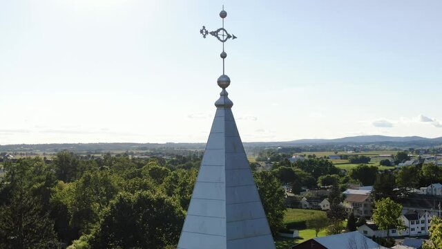 Rising aerial reveals church steeple with weather vane atop, pan reveals rural countryside in Ephrata Lancaster County PA USA