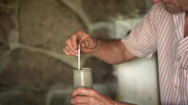 Older winegrower placing glass tube hydrometer into a test jar filled with grape juice.