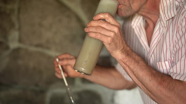 Close up view of older caucasian vintner pulling out hydrometer out of test jar and tasting grape juice.