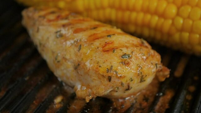 A deliciously seasoned chicken breast in a hot iron grill pan. Burn marks from the pan form a golden brown pattern on the breast. Bubbles from the seasoning sauce can also be seen.