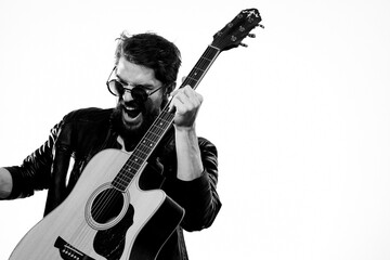 Obraz premium A man holds a guitar in his hands music emotions black leather jacket dark glasses studio light background