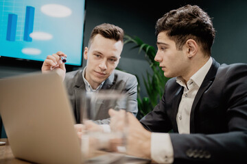They look at the chart and tell each other about their ideas in their heads. they are discussing their next business project. two promising business managers in the new office.