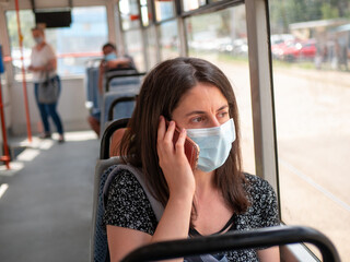 woman using public transport wearing face mask on bus to protect against coronavirus during Covid 19 pandemic