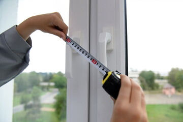 A worker measures the handles of the window frame with a construction tape measure, close-up.