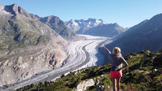 Aletsch Glacier from Moosfluh viewpoint in summer, Valais Canton, Switzerland, Europe. Tourist hiker woman pointing her finger the Alpine glacier. Outdoor activities. Trekking in Swiss Alps.