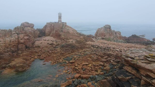 Fly over the rocky coastline of the Brehat island to the Paon lighthouse under misty weather at low tide, Brittany, France