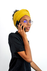Portrait of young woman wearing glasses and yellow head scarf and speaking on mobile phone over white background