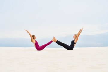 Fototapeta premium Two beautiful young women perform yoga pose navasana