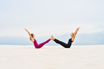 Fototapeta na wymiar Two beautiful young women perform yoga pose navasana