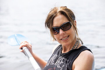 Woman with a boat oar wearing sunglasses outside on a lake