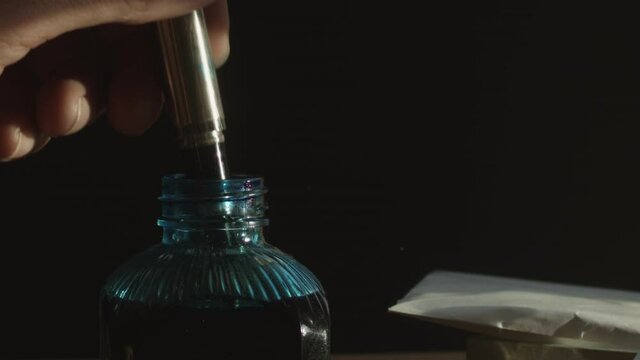 Fountain pen on ink bottle with letters on table as dust floats, pan