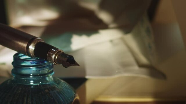 Fountain pen on ink bottle with letters on table as dust floats, pan