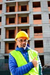 Confident construction engineer in hardhat with thumbs up in front of construction site. Visiting construction site. Portrait of confident elderly construction engineer.