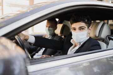 Fototapeta na wymiar businessmen and coronavirus, pandemic, epidemic, infection. Sitting in the car wearing protective masks from covid 19, talking about work, strict business suits