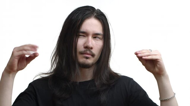 Close-up of handsome east-asian bearded guy with long dark hair and piercing, looking tired and showing blah blah gesture, mocking people who talk, standing over white background