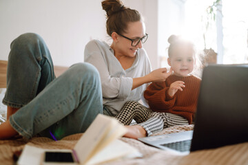 Mother playing with child during working. Busy young woman with daughter in home office. Childcare and work concept. Covid-19.