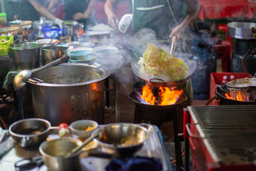 Asian street food festival in city. Chef cooking noodles and vegetables in a pan on fire. Fried chinese japanese noodles with vegetables and shrimps in wok on the open fire