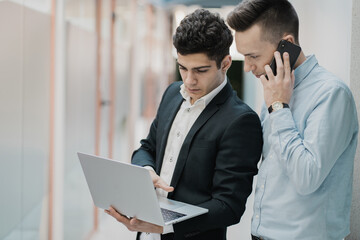 Young male managers work in the office. Daylight laptop in hand shows statistics of past work. Calling all the phone to the director. Caucasian appearance beautiful hairstyles.