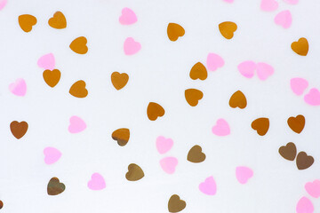 abstract background of chaotically lying confetti f in the shape of a heart of pink and gold colors.