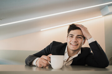 Contented Cheerful happy man of Caucasian appearance sits drinking coffee and looks into the camera in a black stylish business suit.