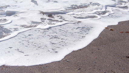 Waves reaching the shore, with sand, sea foam, small stones and seaweed