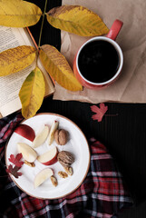 Autumn coffee concept. Flat-lay of plaid shirt, book, mug of coffee and yellow fallen leaves over dark rustic wooden table background, top view, vertical composition