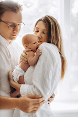 Beautiful parents with newborn baby girl, loving mom hold little daughter in arms, caring husband gently hug adorable wife, smiling, enjoy tender family moments, parenting concept