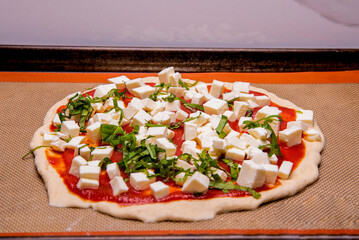 Uncooked cheese and basil pizza on sheet pan preparing to be cooked
