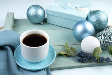 Winter berries on a branch with a gift box, a Cup of coffee, and Christmas balls on a soft blue tray. The concept of the new year 2021 and Christmas.