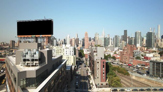 Dolly drone shot from NY on a perfectly clear summer day down a street with the NYC skyline as the backdrop. In the foreground is a blacked out billboard perfect for overlaying a graphic for an intro.