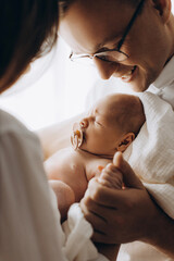 Portrait of beautiful little daughter with happy parents, loving father hold cute newborn baby girl in arms, smiling, enjoy tender family moments, parenting concept