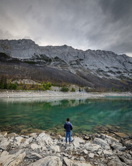 A man stands over the rocks loking at the mountains on the shore of Medicine Lake (Jasper, Alberta, Canada)