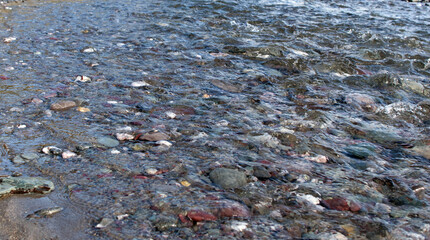 Clear fresh fast moving water flowing over beautiful flat pebbles towards the sea.
