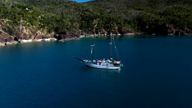 Wide rotating drone shot of sailboat in bay at Hook Island with people on deck. Near Whitsunday Island Australia