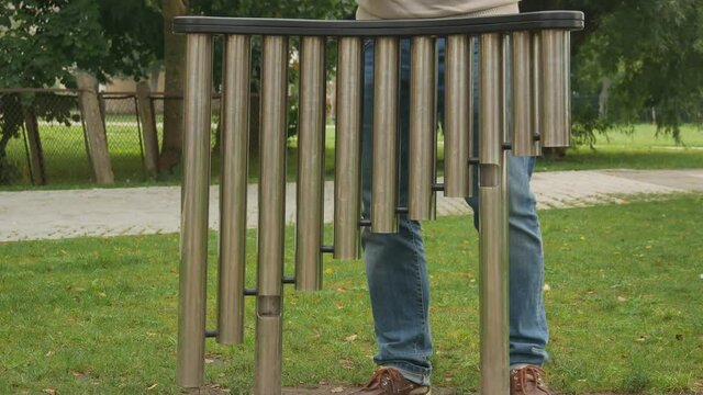 A Man Plays Hanging Percussion Pipe Tubes In Public Urban Space.