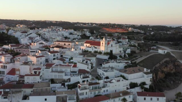 Birds Circle over Mesmerizing European Riverfront Hilltop town Ferragudo during Amazing Sunset, Drone Aerial Pullback
