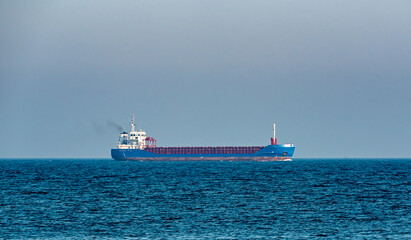 Blue cargo ship sailing on the ocean at a distance.