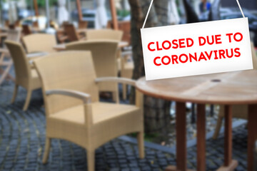 Closed due to CORONAVIRUS sign in red letters ON a white background with a blurry cafe background in the background