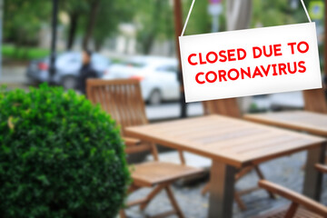 Closed due to CORONAVIRUS sign in red letters ON a white background with a blurry cafe background in the background