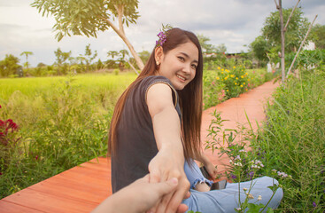 Young woman are smiling sitting on wooden bridge holding hands with someone and rice field in farm and flowers. Relax on vacation concept. Holiday with natural.