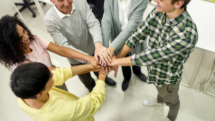 Cropped shot of group of diverse employees putting their hands on top of each other like a real team while standing in the office, Aged woman and man, senior interns having first day at work
