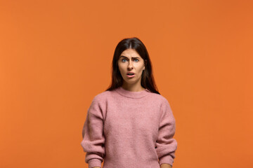 Fototapeta premium Are you serious. Portrait of shocked stunned beautiful woman in pink sweater, looking dissatisfied and surprised. On orange background