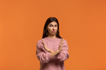 Ugh i won't it. Portrait of serious woman in pink sweater, makes denial hand gesture, keeps arms crossed over chest, demonstrates stop sign, says no to something or somebody. on orange background