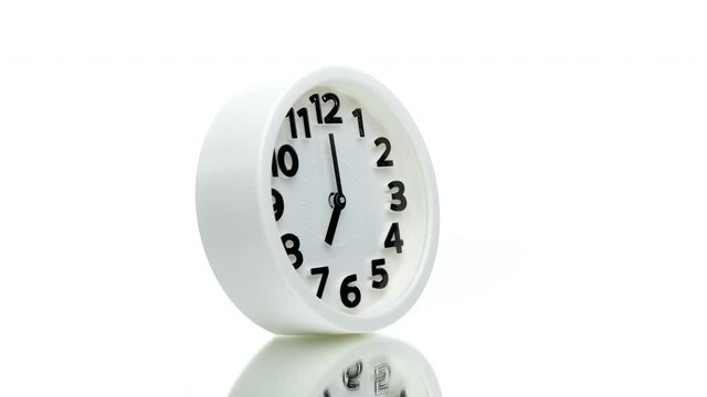 White round alarm clock showing seven o'clock spinning rotating 360 isolated on white background. Waking up for work in morning concept