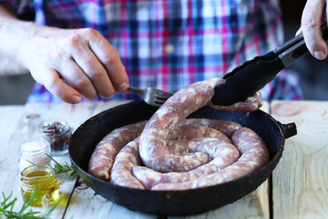 Selective focus. The chef puts raw sausages in a frying pan. Bavarian homemade sausages. Raw pork sausages.