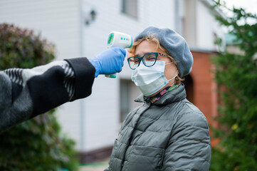 A doctor measures the temperature of an elderly woman wearing a mask with a non-contact infrared...