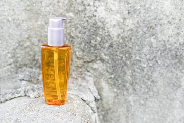 An orange oil bottle next to natural stones against a gray wall with natural light. Trendy style. Cosmetic mockup. Copyspace.