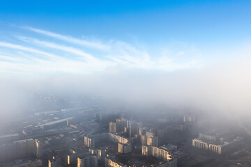 The city is under a layer of fog and low clouds, from above there is a clear blue sky.