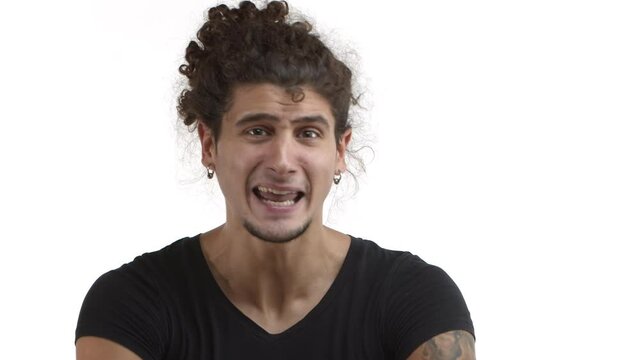 Close-up of handsome latino guy with curly ponytail and earrings gesturing and rapping, trying to convince someone, standing over white background in black casual t-shirt