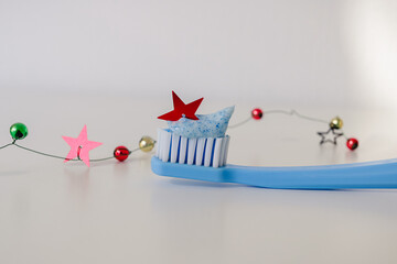Light blue toothbrush with toothpaste decorated with a red sequin star on a white background with handmade decorative garland. Dental medical Christmas  concept. Merry Christmas from dentist.